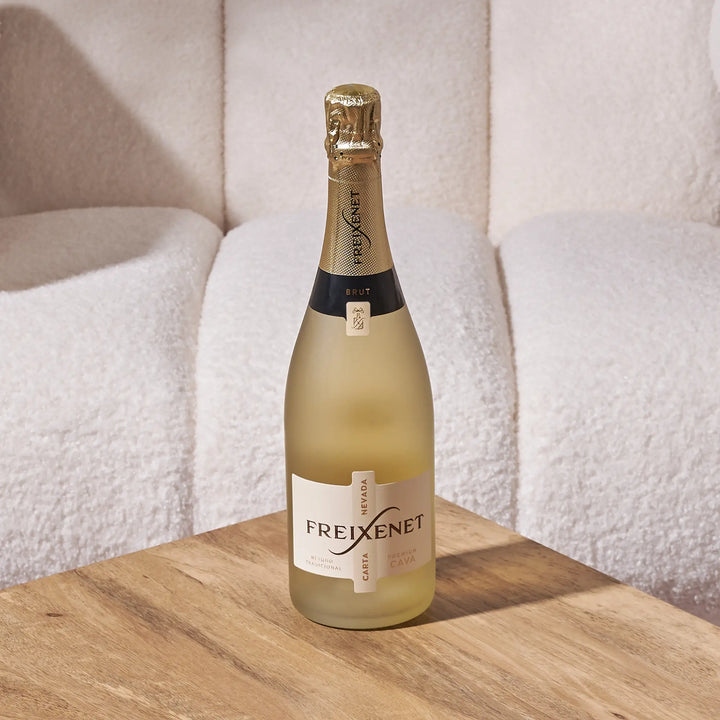 Freixenet Carta Nevada Brut Cava bottle on a wooden table with a soft, neutral background