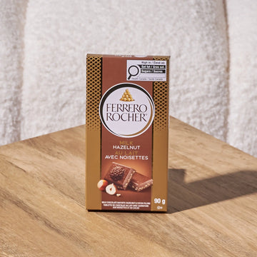 Ferrero Rocher hazelnut milk chocolate bar on a wooden surface with a textured white background