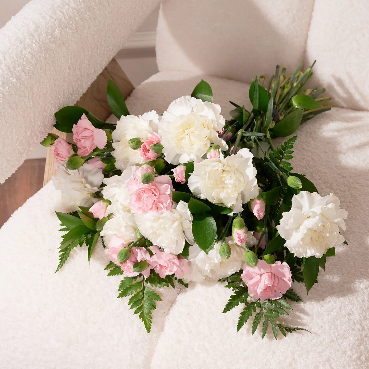 A bouquet of artificial white and pink flowers with green foliage arranged on a cream-colored armchair.