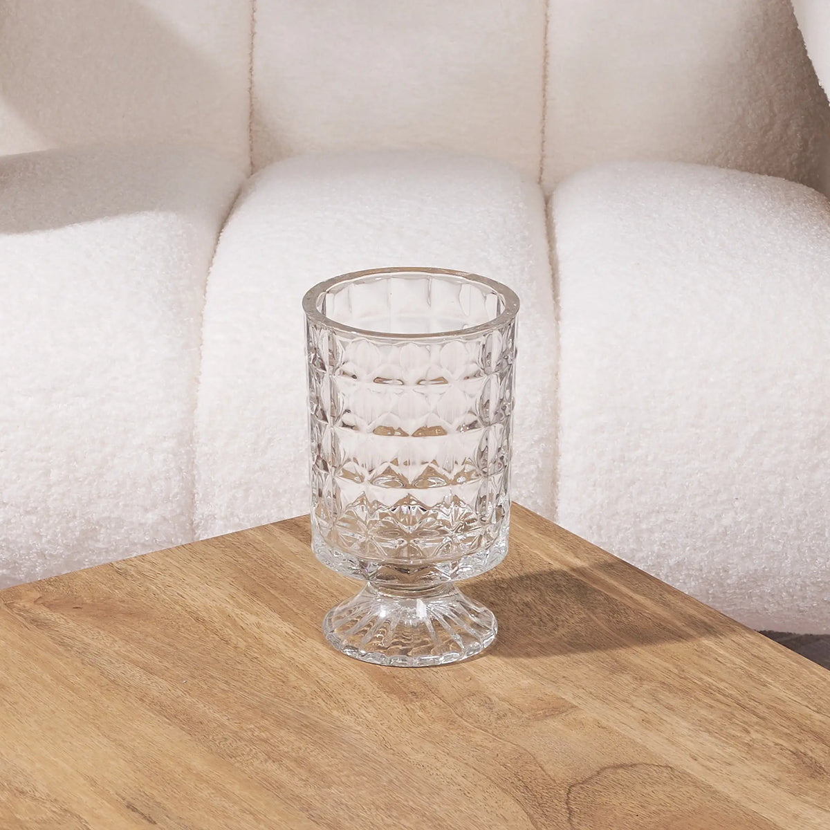 short clear glass vase on a wooden table with a white sofa in the background