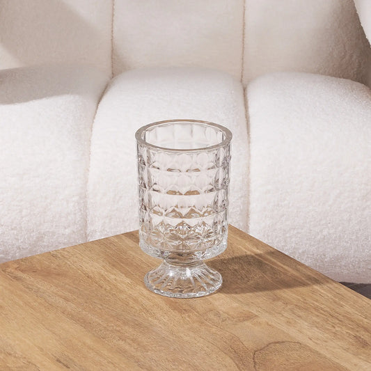 short clear glass vase on a wooden table with a white sofa in the background