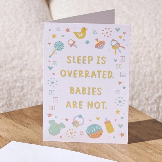 A baby nursery greeting card with the text 'SLEEP IS OVERRATED. BABIES ARE NOT.