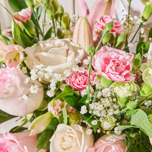 A closeup shot of a  of bouquet of pink and white roses, lilies, and mixed greeneries