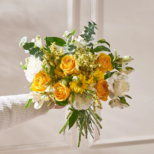 Bouquet of yellow and white flowers held by a person against a neutral background