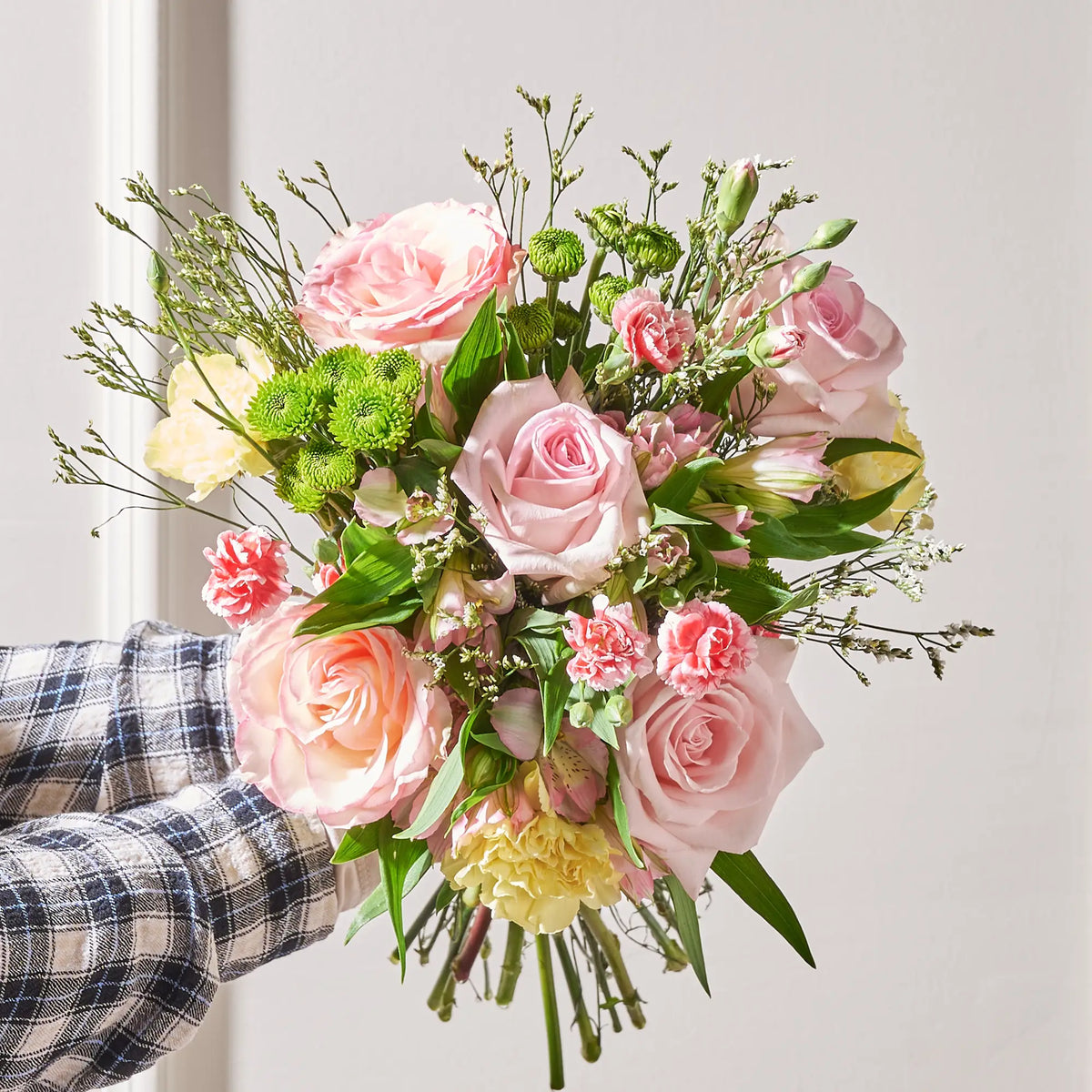 Bouquet of pink roses and greenery held by a person wearing a plaid shirt.