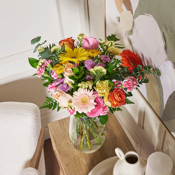 Bouquet of colorful flowers in a clear vase on a wooden table.
