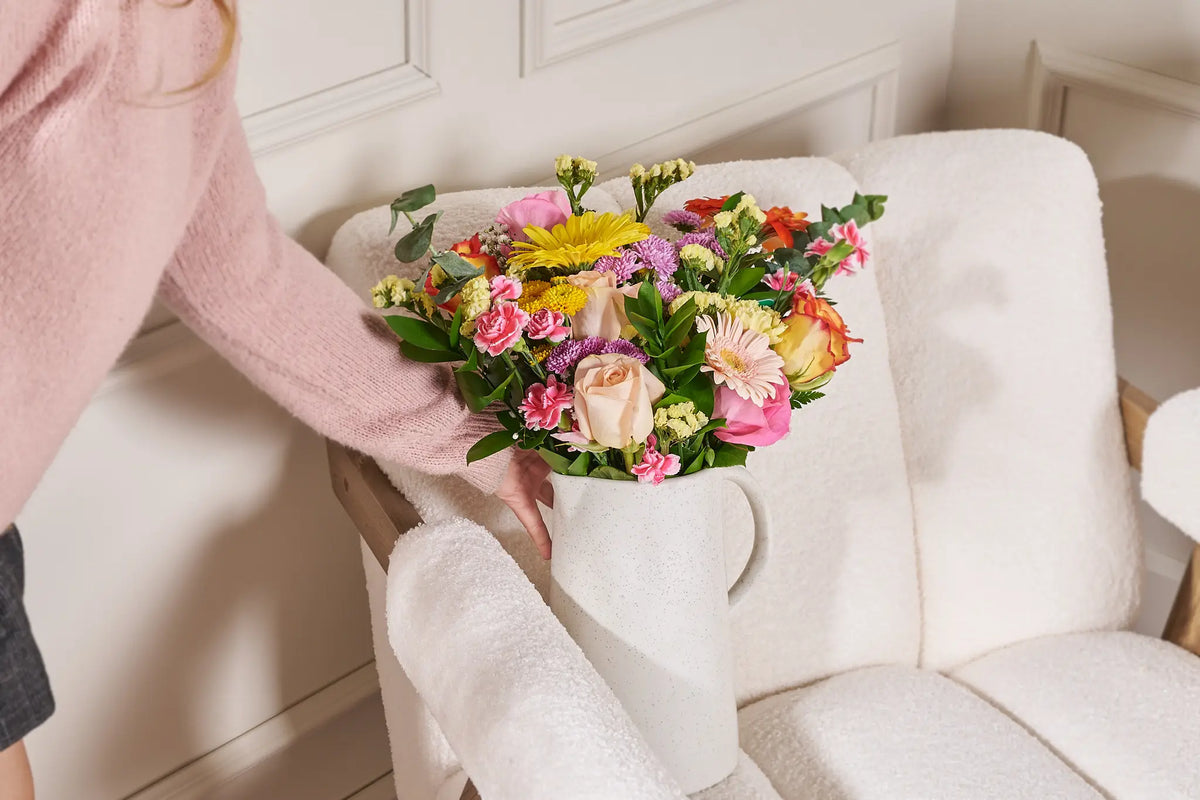 Person holding a colorful bouquet of flowers on a white couch.