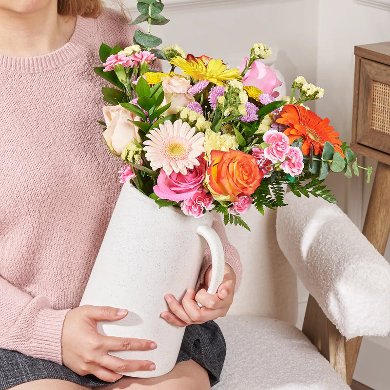 Person holding a colorful bouquet of flowers in a white vase.
