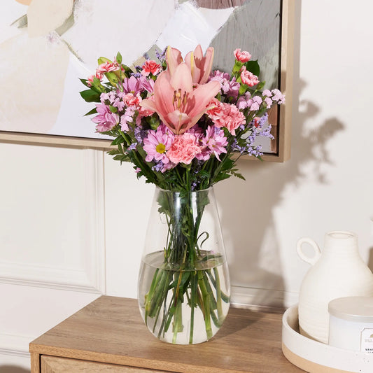 Bouquet of pink and purple flowers in a clear vase on a wooden table.