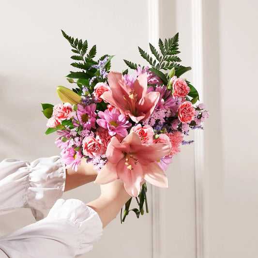 Bouquet of pink flowers held by a person wearing a white shirt against a light background