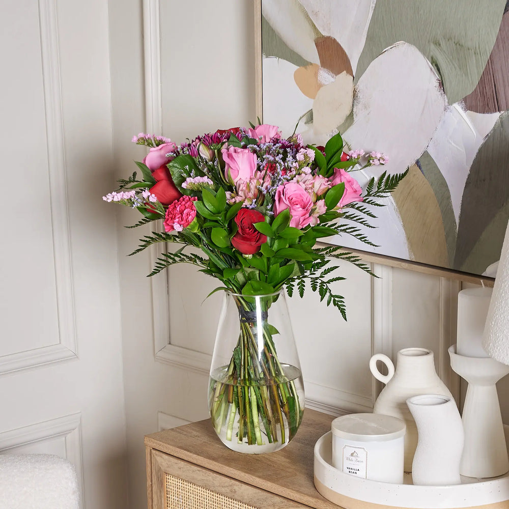 Bouquet of flowers in a clear vase on a wooden cabinet with decorative items.